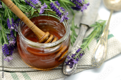 Lavender honey in a glass with flower pot of Lavandula stoechas and antique silverware.