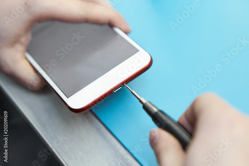 Cropped indoor view of unknown repairman opening faulty smart phone using precision screwdriver. Hands of male technician holding opening tool and generic electronic communication device in lab