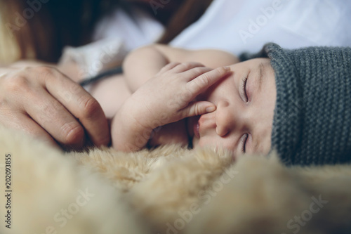 Newborn baby girl sleeping lying on a blanket on the bed next to her mother's hand