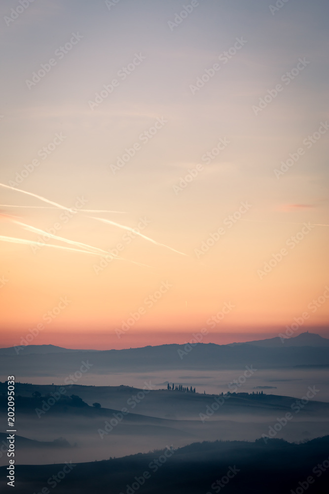 Only few seconds before the sunrise in Tuscany, Italy. Misty morning with light fog shapes magically the hills and valleys of this beautiful picturesque travel location