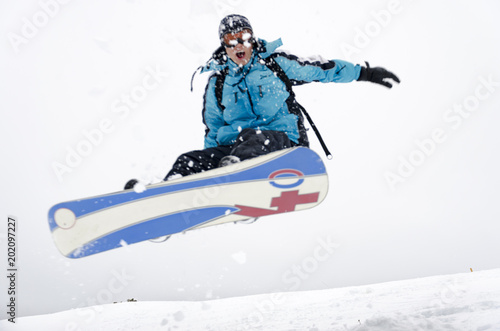 Snowboarder jumping through air with gray sky