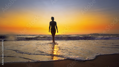 Beach woman running out of water at sunset enjoying freedom during summer holidays vacation travel. Beautiful happy free mixed race Caucasian female girl