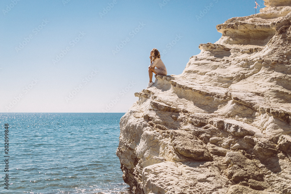 the girl sits on a white rock near the sea