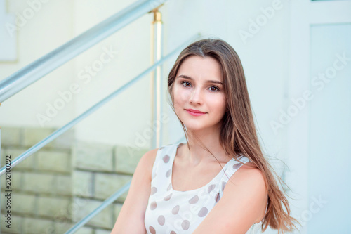 Teen girl with long brunette hair smiling sitting on steps.