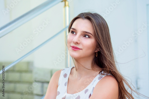 Teen girl with long hair sitting on steps looking up to side.