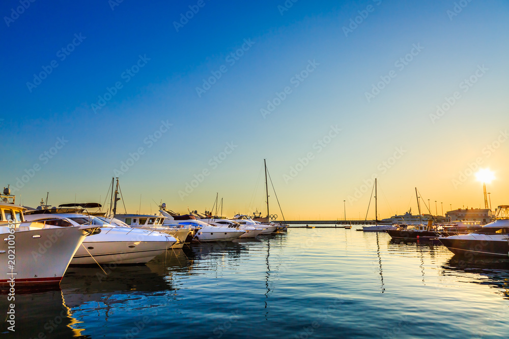 Luxury yachts, sailing and motor boats docked in sea port at sunset.