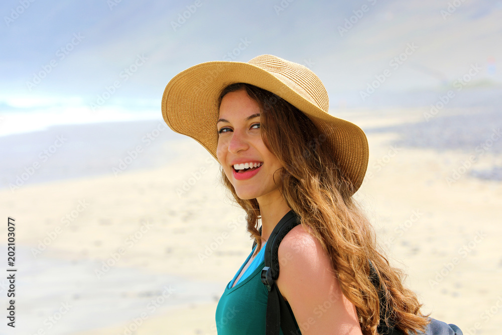 Adventure girl with backpack and straw hat looking to the camera. Young woman exploring Canarian Coast with sand dunes of Lanzarote, Spain.