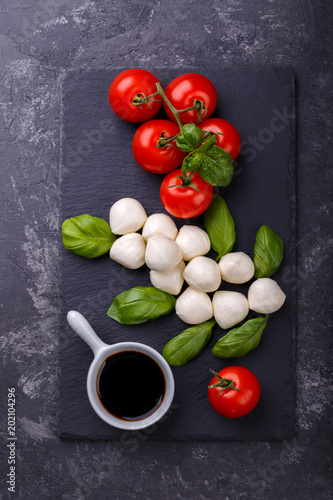 Mozzarella cheese, basil and tomato cherry on slate stone board, copy space. Ingredients for Caprese salad