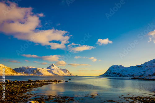 Fototapeta Naklejka Na Ścianę i Meble -  Sunset at Henningsvaer shoreline with huge mountains covered with snow in a gorgeous blue sky on Lofoten Islands, Austvagoya