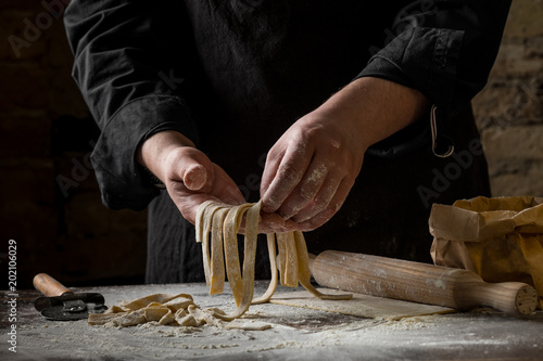 Chef cook hands holding sliced pastry for pasta over wooden table on brick wall background, home cooking concept.