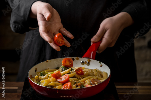 Close-up of a chef preparing an Italian penne pasta on a red frying pan close-up. The concept of flying products.