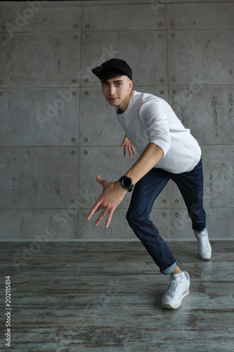 Teenager guy in baseball cap and white sneakers, jeans and white sweater dancing hip-hop. Dynamics of modern dance movement. Youth fashion.