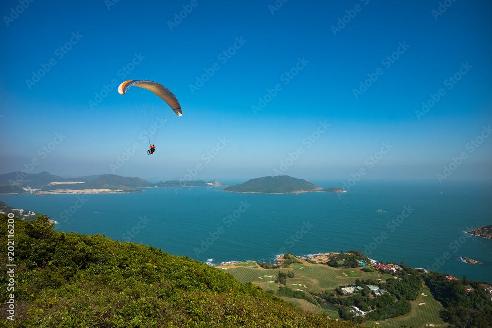 Tandem paragliders having fun paragliding over Dragon's Back hiking trail in Hong Kong, Asia Tandem paragliders having fun paragliding over Dragon's Back hiking trail in Hong Kong, Asia