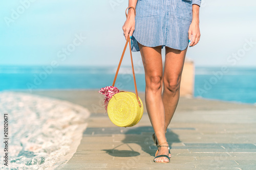 Woman hands with fashionable stylish rattan bag and silk scarf on the ocean background. Tropical island of Bali, Indonesia. Rattan handbag and silk scarf. photo