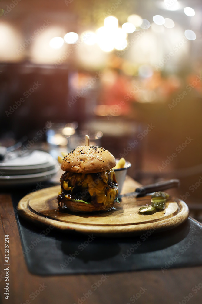 Homemade double cheese burger meat with pickle on wood plate. Delicious menu in rustic restaurant with bokeh light background.