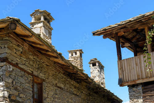 Old authentic rustic houses made of stone bricks and stone slate roofs in Kovachevitsa, Bulgaria against cloudless sky in sunny day photo