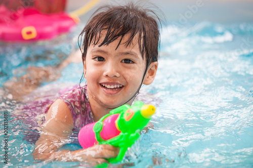 Happy asian little child girl having fun to play water gun and swimming in the pool in Songkran festival Thailand