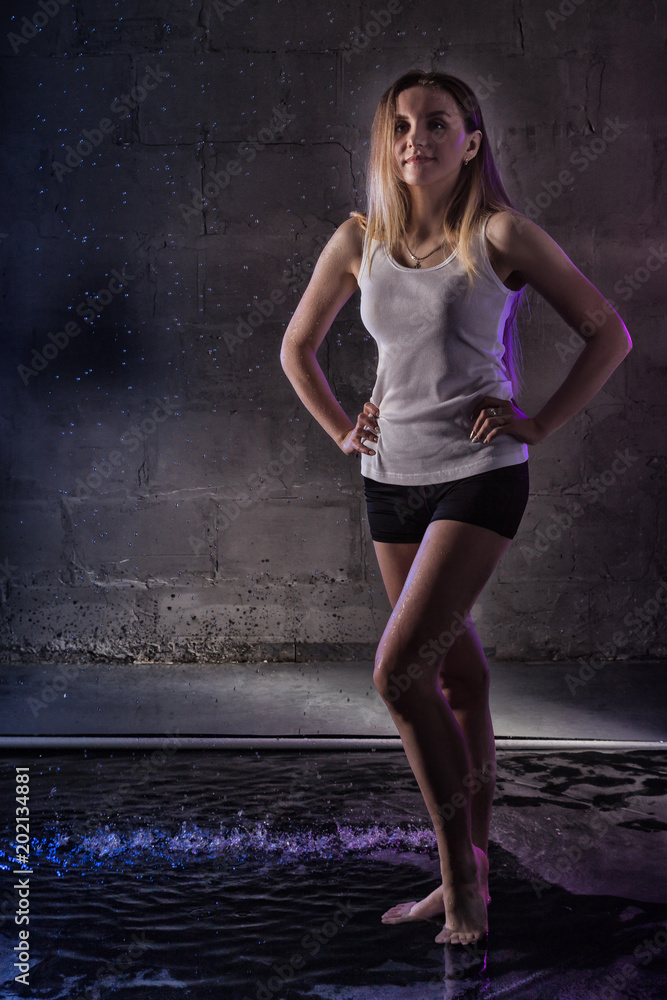 Fototapeta premium Portrain of the girl in the white shirt with water drop in a dark room illuminated by light during a photoshoot with water
