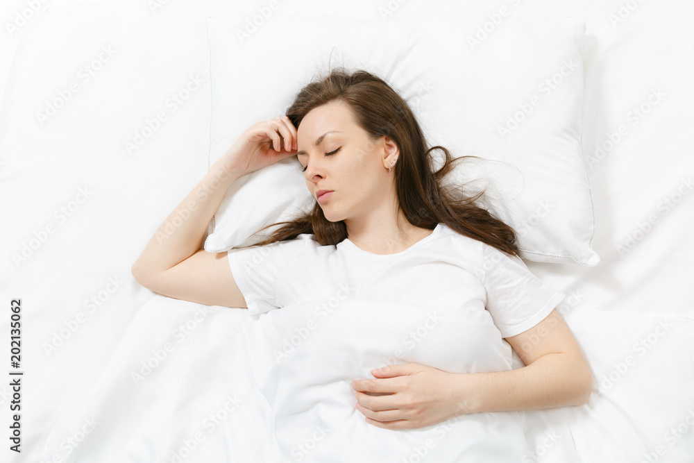 Top view of happy calm brunette young woman lying in bed with white sheet, pillow, blanket. Sleeping pretty female spending time in room. Rest, relax good mood concept. Copy space for advertisement. Top view of happy calm brunette young woman lying in bed with white sheet, pillow, blanket. Sleeping pretty female spending time in room. Rest, relax good mood concept. Copy space for advertisement.