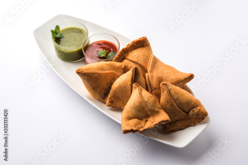 Veg Samosa is a triangle shape pakora stuffed with Aloo sabji, served with green chutney and tomato sauce. selective focus
