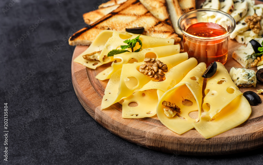 Cheese plate: Parmesan, cheddar, gouda, mozzarella and other with basil on wooden board on dark background with place for text.Honey and Crackers Cheese plate: Parmesan, cheddar, gouda, mozzarella and other with basil on wooden board on dark background with place for text.Honey and Crackers