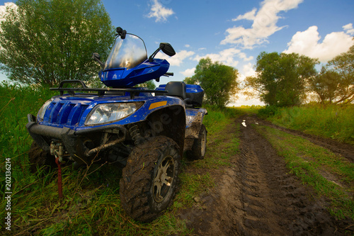 An ATV stands on the roadside of the dirt road in the field against the sunset.