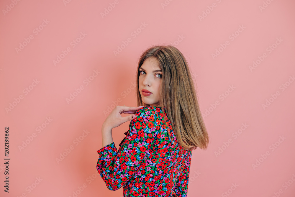 a young girl with long hair and pouting lips, in a beautiful dress and long hair, stands on a pink background in a photo studio, half-turn a young girl with long hair and pouting lips, in a beautiful dress and long hair, stands on a pink background in a photo studio, half-turn