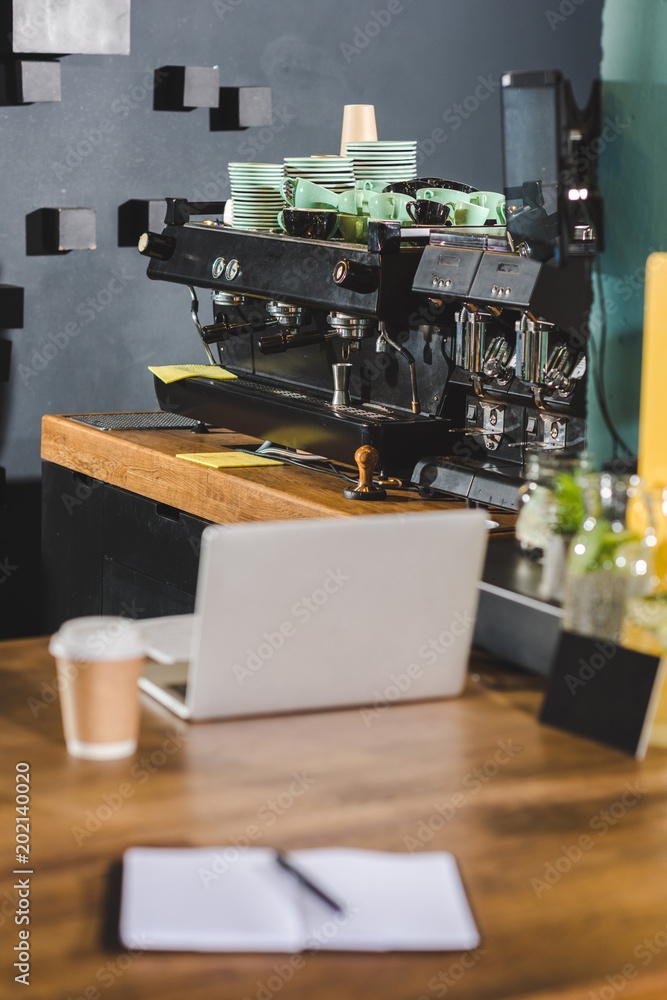 interior of modern cafe with coffee machine,laptop, paper cup of coffee and textbook on table interior of modern cafe with coffee machine,laptop, paper cup of coffee and textbook on table