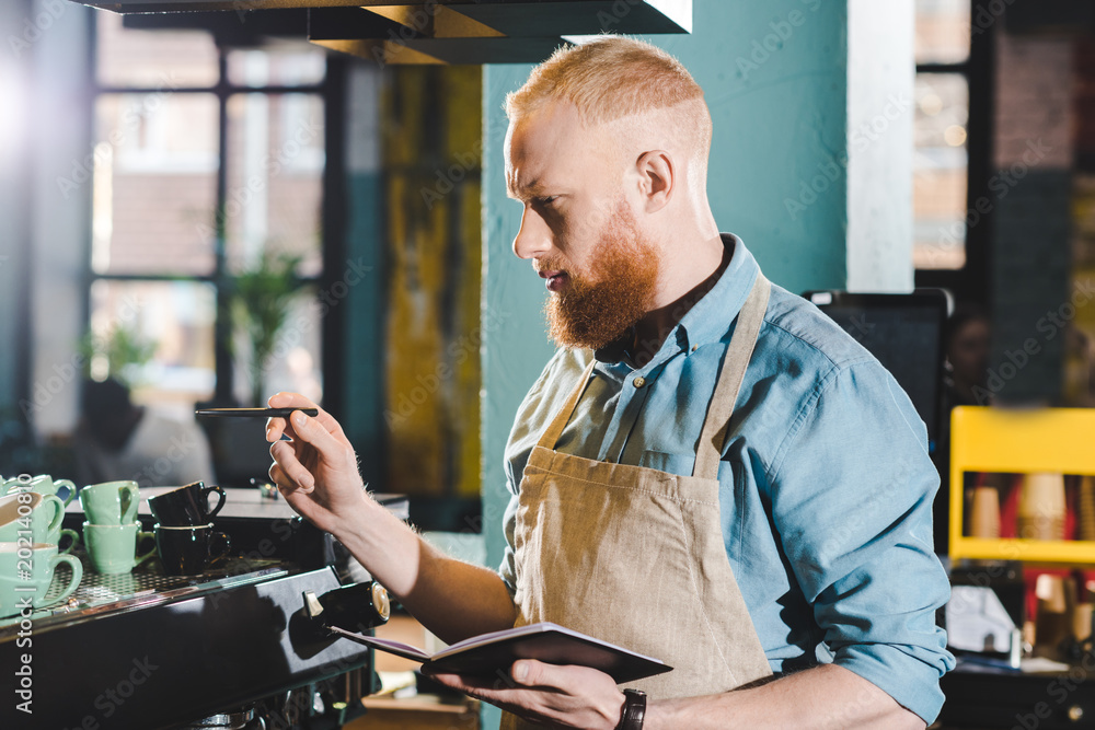 young male barista standing in coffee shop with textbook young male barista standing in coffee shop with textbook