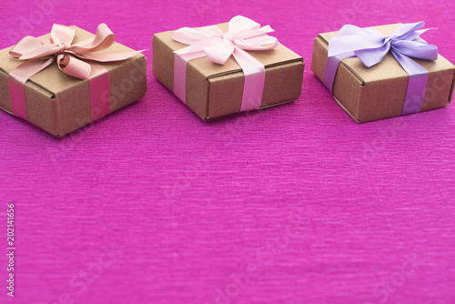 Festive composition three Kraft boxes with gifts on bright pink background.