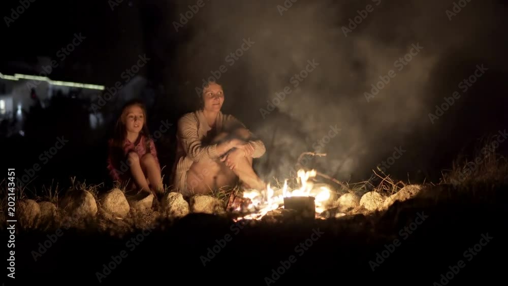 Mother with daughter warm near campfire at night and have conversation Mother with daughter warm near campfire at night and have conversation