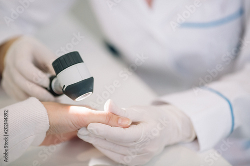 Closeup of dermatologist examining mole on hand of female patient in clinic photo