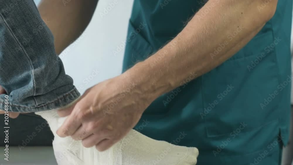 Surgeon putting cast gypsum on patients broken leg, first aid clinic, close-up Surgeon putting cast gypsum on patients broken leg, first aid clinic, close-up