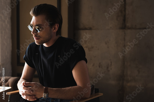 handsome young man in black t-shirt and sunglasses sitting on chair