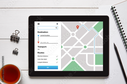 Location tracker concept on tablet screen with office objects on white wooden table. GPS map navigation app. Flat lay