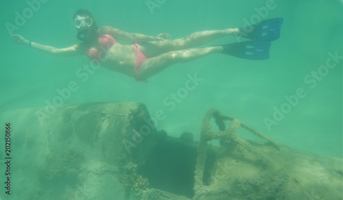 UNDERWATER  Young woman explores remnants of airplane and looks into camera.