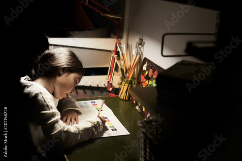 High angle view of girl studying while sitting at illuminated desk in darkroom