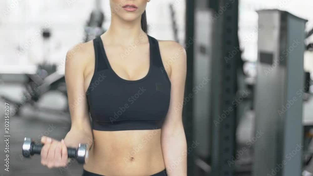 Strong willed woman doing alternating dumbbell curl in gym, workout program Strong willed woman doing alternating dumbbell curl in gym, workout program