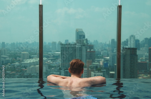 A man from back looking at amazing view of Bangkok from turqouise swimming pool