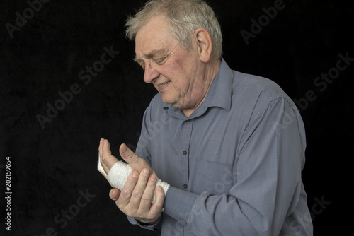 Mature man in pain and holding a bandaged hand, taken on a black background 