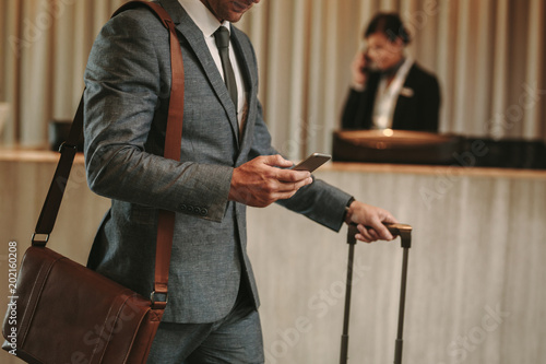 Businessman in hotel lobby with phone and luggage