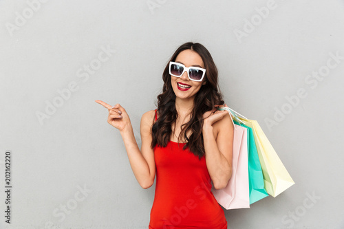 Pleased brunette woman in casual clothes and sunglasses holding packages