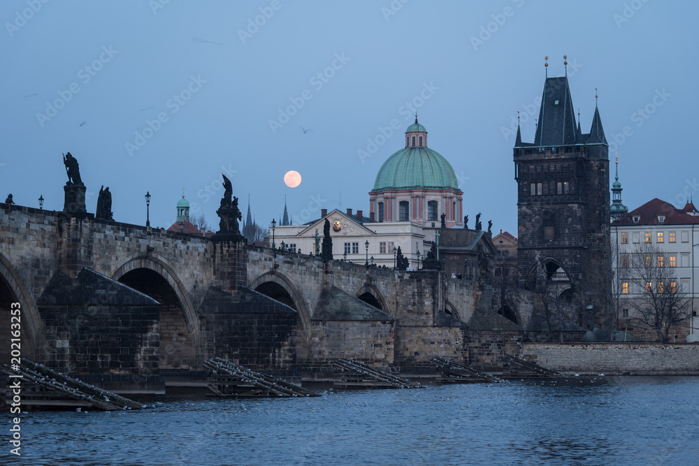 The moon rises over the famous Charles bridge in Prague old town in Czech Republic capital city during twilight