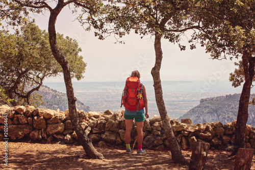 A tourist girl with orange backpack enjoys view of the sea and landscape from the mountain in Mallorca, Spain GR221 photo