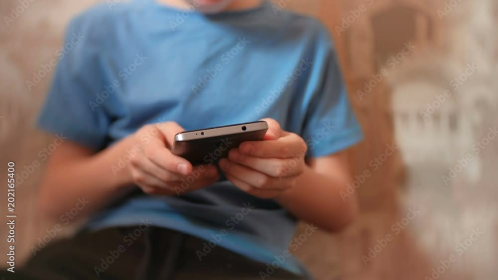 Unrecognizable seven-year-old boy browsing internet on his mobile phone. Unrecognizable seven-year-old boy browsing internet on his mobile phone.