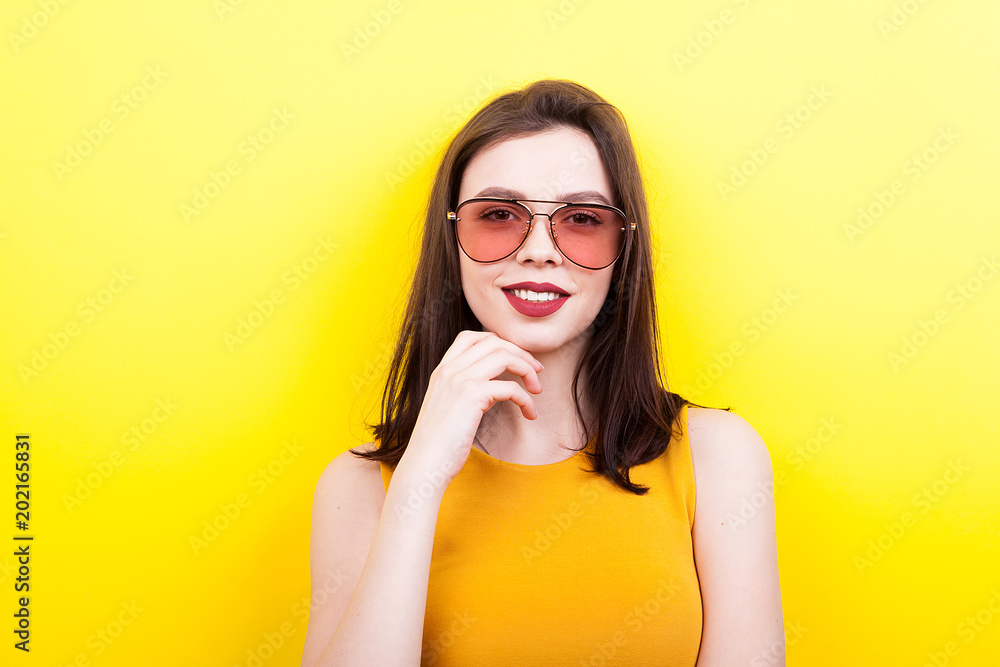 Fototapeta premium Sexy woman wearing sunglasses smiling to the camera on yellow background