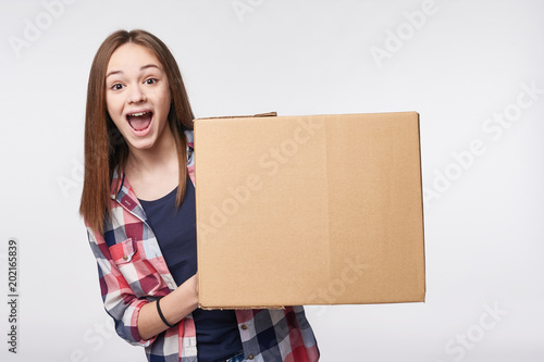 Delivery, relocation and unpacking. Excited young woman holding cardboard box, looking at camera, screaming of joy, isolated