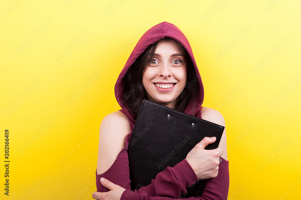 Portrait of woman holding a black folder in hands on yellow background in studio Portrait of woman holding a black folder in hands on yellow background in studio