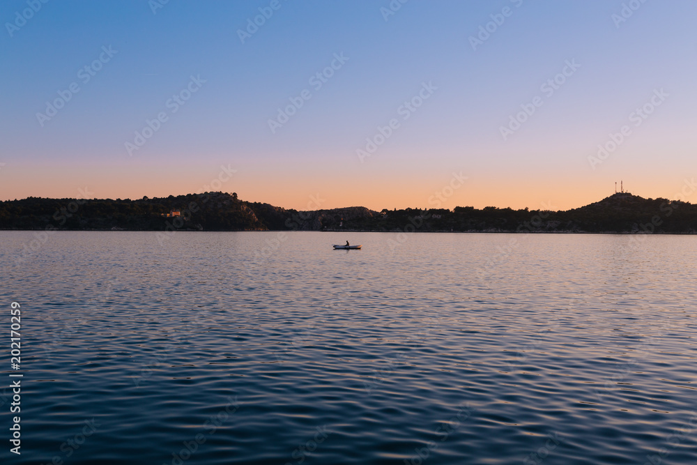 Minimalistisch - Sonnenuntergang über dem Meer mit Bergsilhouette mit Boot Sportler