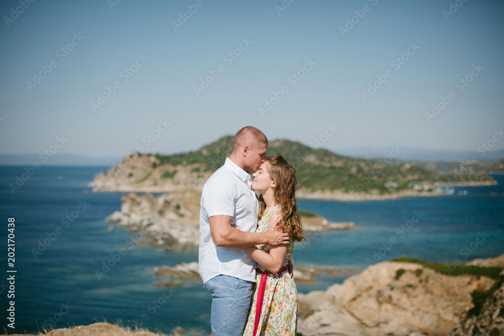 Romantic young couple standing on the top of the mountain with breathtaking view. Man kissing his woman on forehead. Greece